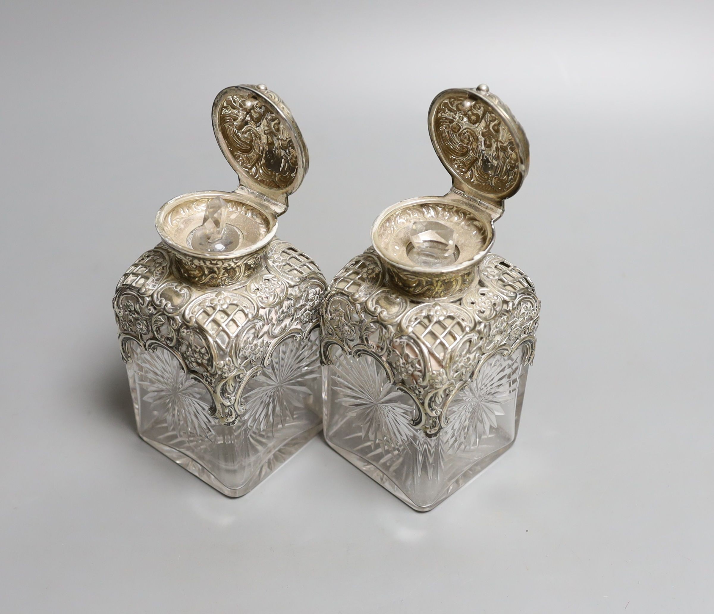 A pair of late Victorian repousse silver mounted cut glass scent bottles with stoppers, William Comyns, London, 1898, height 14.3cm.